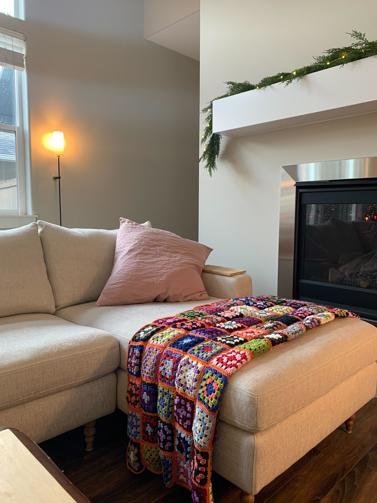 Handmade blanket made of rainbow colored grannie squares draped over the edge of a beige couch.