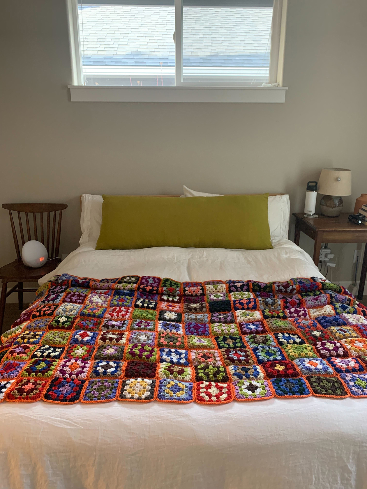 Handmade blanket constructed of colorful grannie squares draped over the back of a leather chair in a living room.