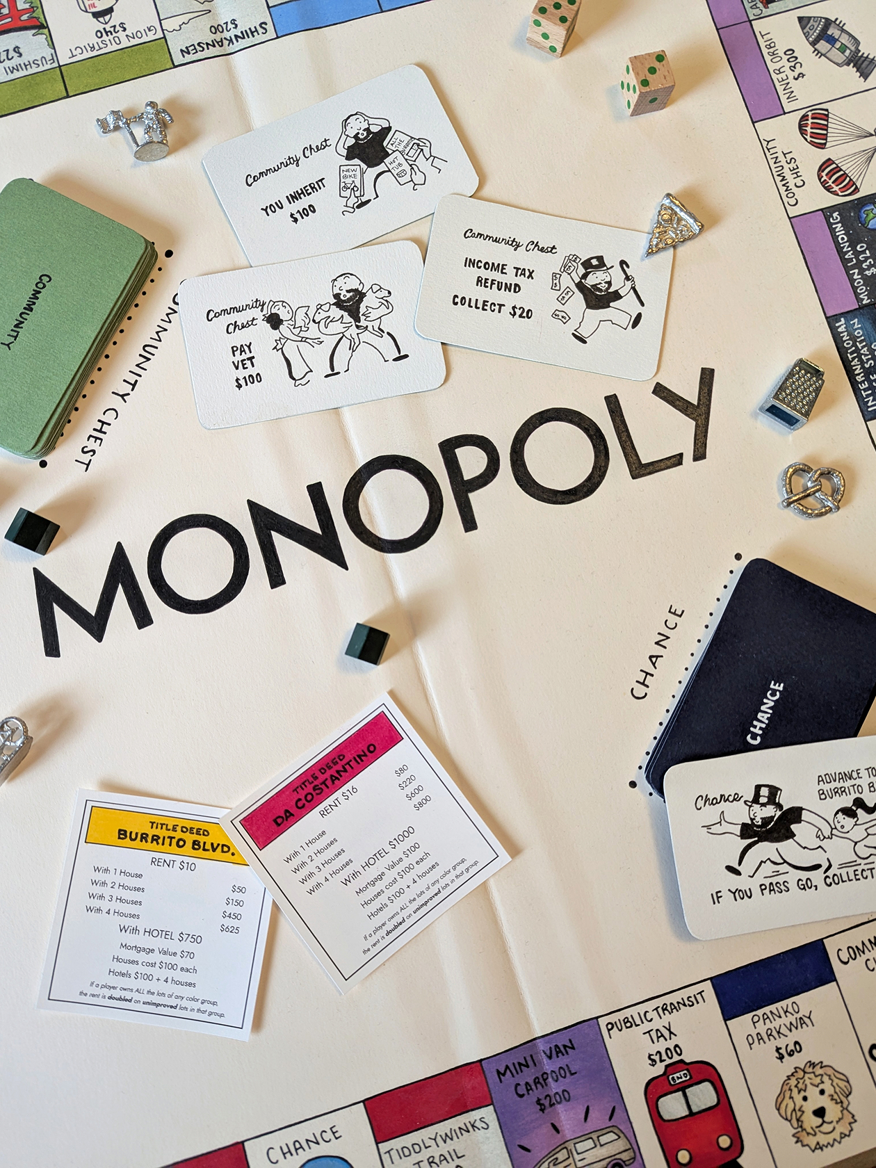 Details of a handmade monopoly game board, including silver game pieces and hand illustrated chance and community cards.